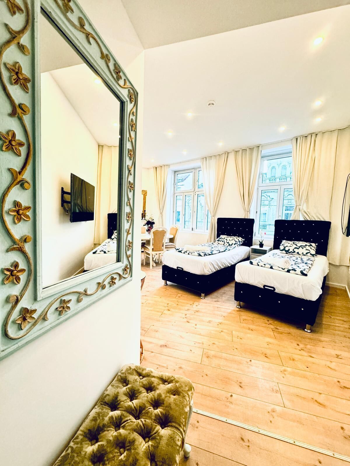 A bedroom with two beds, a large mirror, and a tufted ottoman.