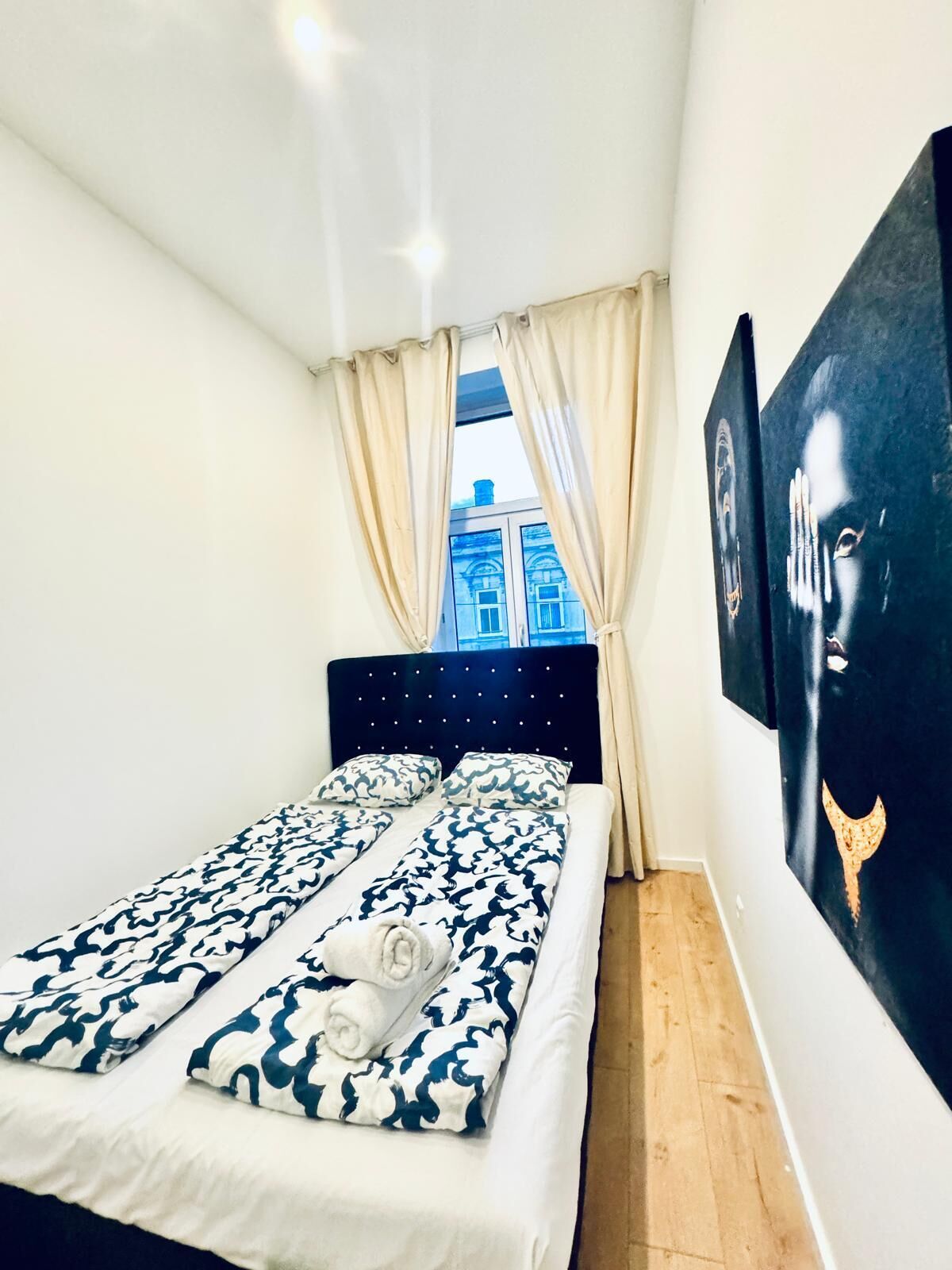 Quarto pequeno e moderno com cama, cortinas e uma pintura grande na parede.