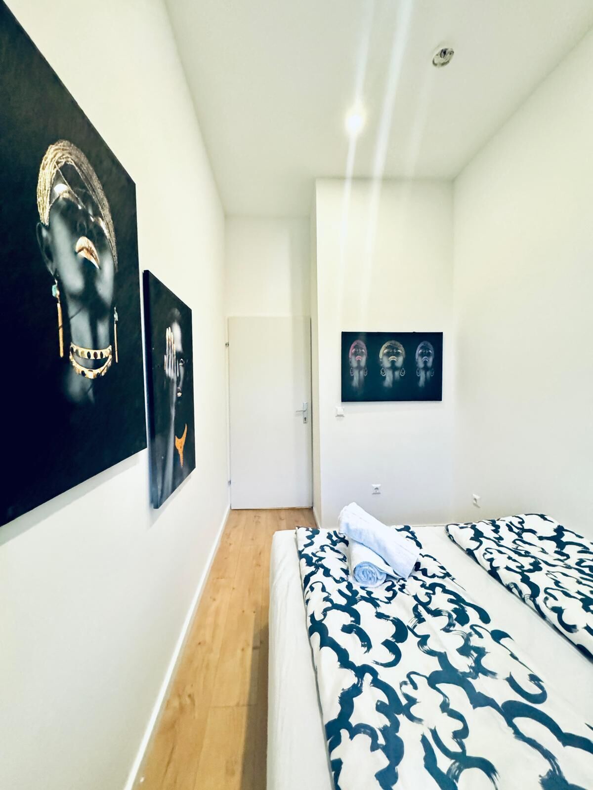 A bedroom with a bed, a door, and two artworks on the wall.