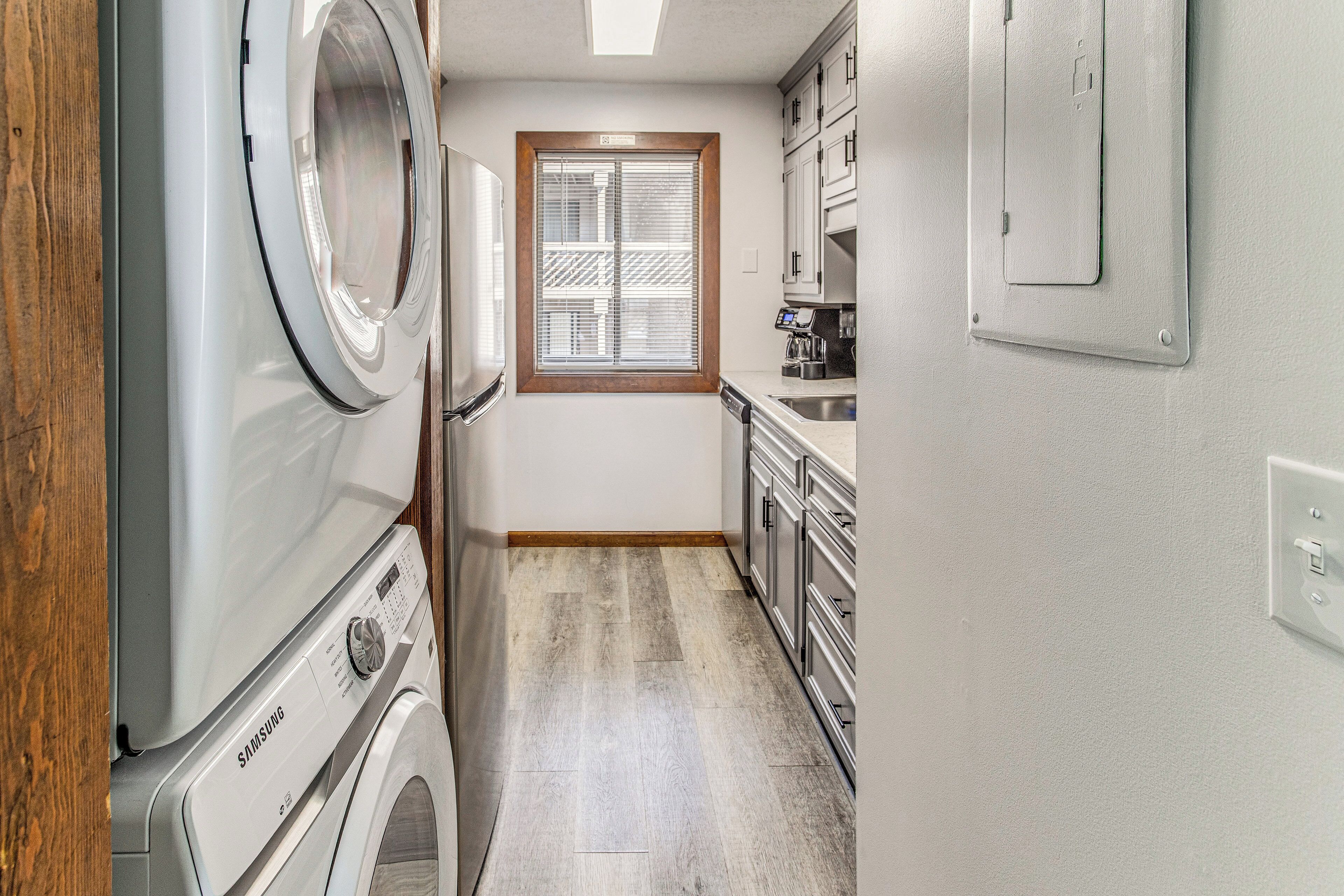A laundry room with a Samsung washer and dryer, a window with blinds, and a kitchen area with a sink and cabinets.