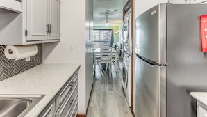 A kitchen with a stainless steel refrigerator, a washing machine, and a dining area with a table and chairs. - Walk to Ocean: Condo w/ 3 Pools in Myrtle Beach (Myrtle Beach)
