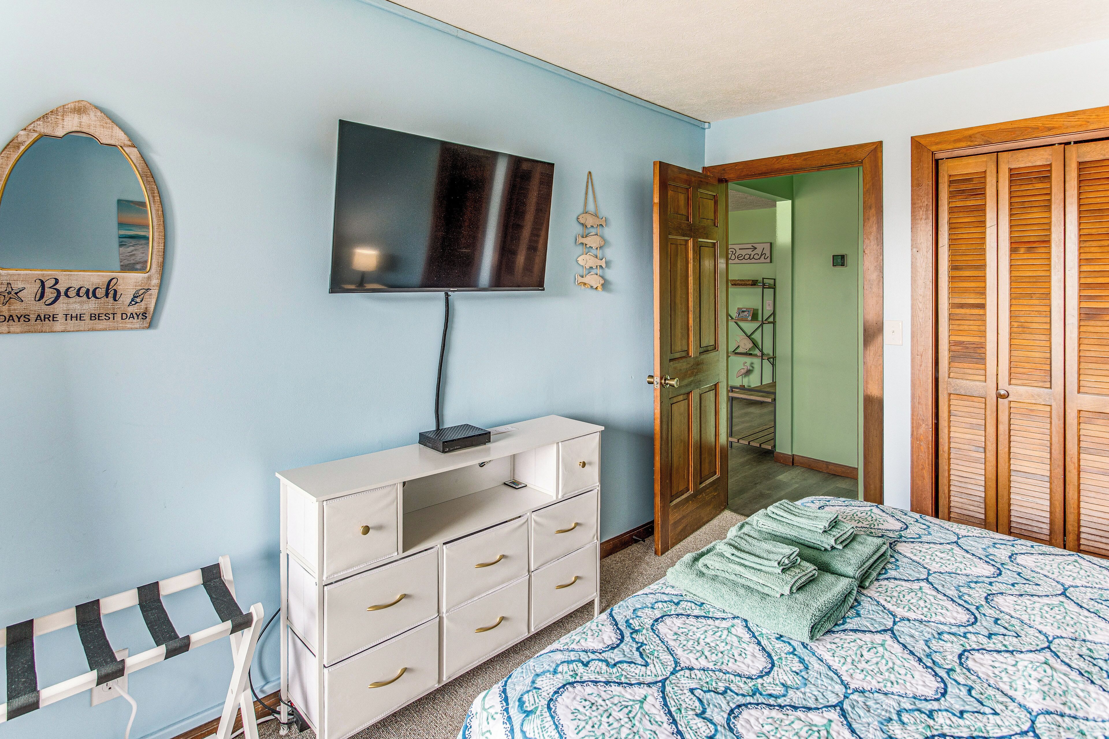 Ein Schlafzimmer mit Bett, Kommode, Fernseher und einer Tür zum Badezimmer.