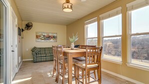 A dining area with a wooden table and chairs, a painting on the wall, and a view through large windows. - On Thousand Hills Golf Course: Condo w/ Sunroom (Branson)