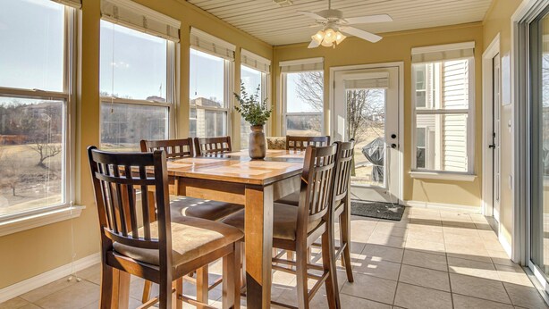 A sunlit dining area with a wooden table and chairs, large windows, and a ceiling fan. - On Thousand Hills Golf Course: Condo w/ Sunroom (Branson)