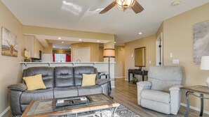 A living room with a leather sofa, a grey armchair, a coffee table, a ceiling fan, and a kitchen area in the background. - On Thousand Hills Golf Course: Condo w/ Sunroom (Branson)