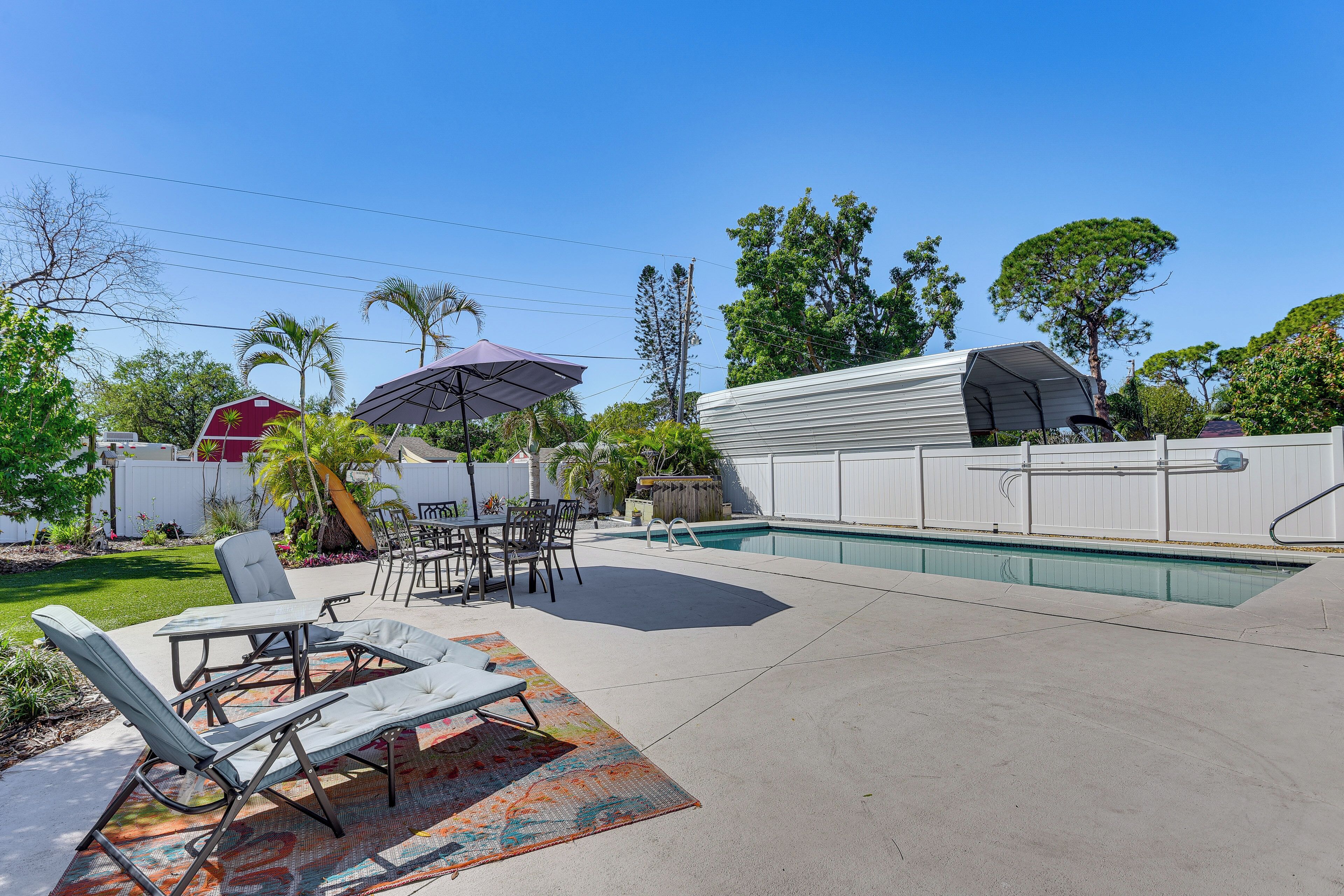 A backyard with a pool, lounge chairs, a dining table, and a covered patio area.