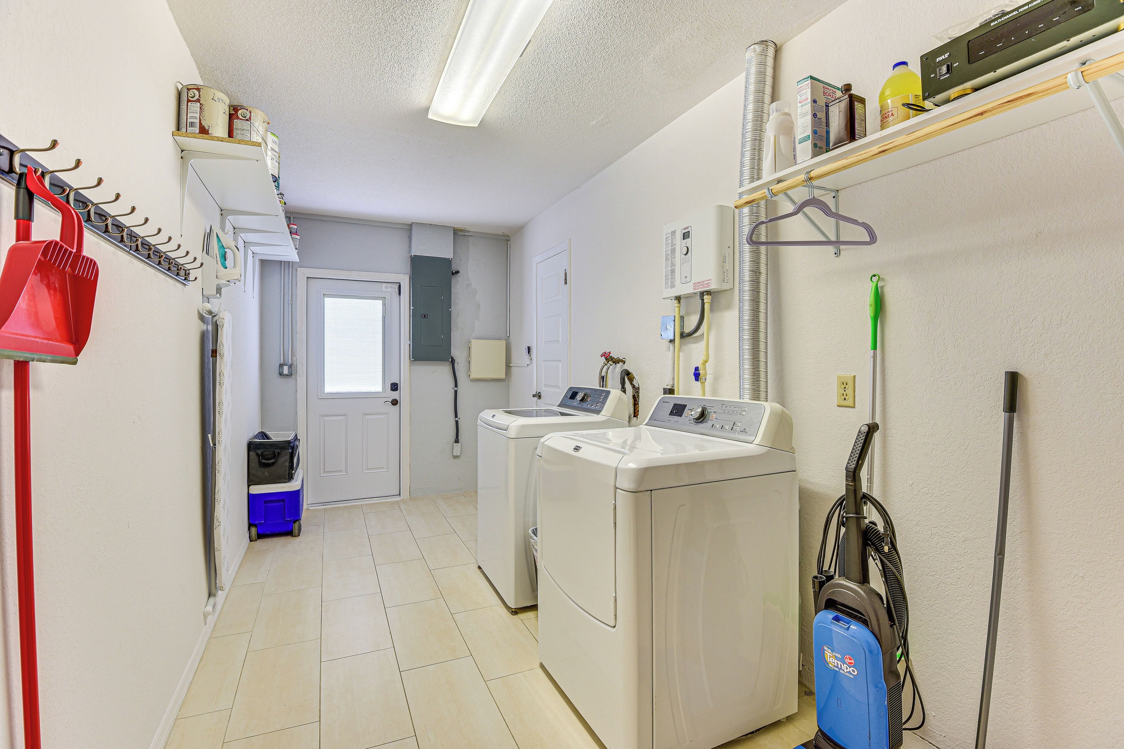 A laundry room with two washing machines, a vacuum cleaner, and a red mop.