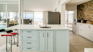 A modern kitchen with a large island, white cabinetry, and a view to the outside. - 3bed With Indoor Pool and Sea Views The Sanctuary (Cape Town)