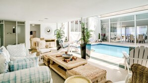 A modern living room with a pool view, wicker furniture, and a large mirror. - 3bed With Indoor Pool and Sea Views The Sanctuary (Cape Town)