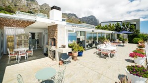 A modern outdoor patio with a stone fireplace, white furniture, and potted plants. - 3bed With Indoor Pool and Sea Views The Sanctuary (Cape Town)