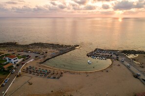 An aerial view of a coastal area with a beach, a pier, and a parking lot.