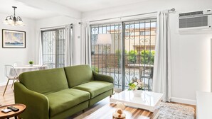 Ένα σαλόνι με έναν πράσινο καναπέ, ένα λευκό τραπεζάκι σαλονιού και θέα σε ένα μπαλκόνι με κάγκελα.