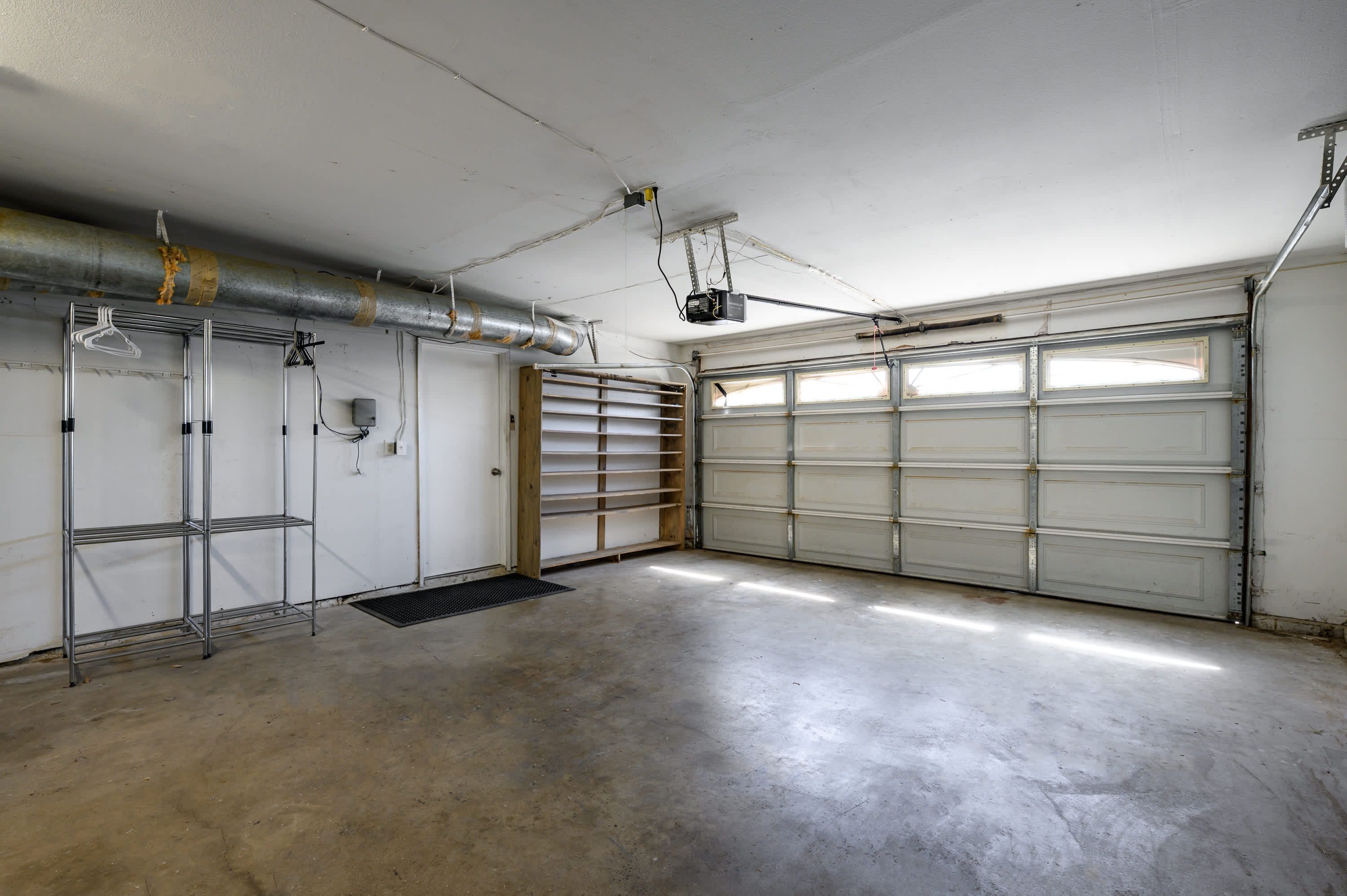 A garage with a concrete floor, metal shelving, a vent, and a closed garage door.