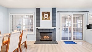 A living room with a fireplace, a dining area with chairs, and a sliding glass door leading to a patio.