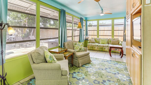 A spacious living room with a green and blue color scheme, featuring a sofa, armchairs, a coffee table, and a ceiling fan. - 4 Mi to Beaches: Vibrant Stuart Villa w/ Patio! (Stuart)