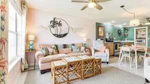 A living room with a sofa, a coffee table, and a dining area with chairs. There is a ceiling fan and a kitchen in the background. - 4 Mi to Beaches: Vibrant Stuart Villa w/ Patio! (Stuart)
