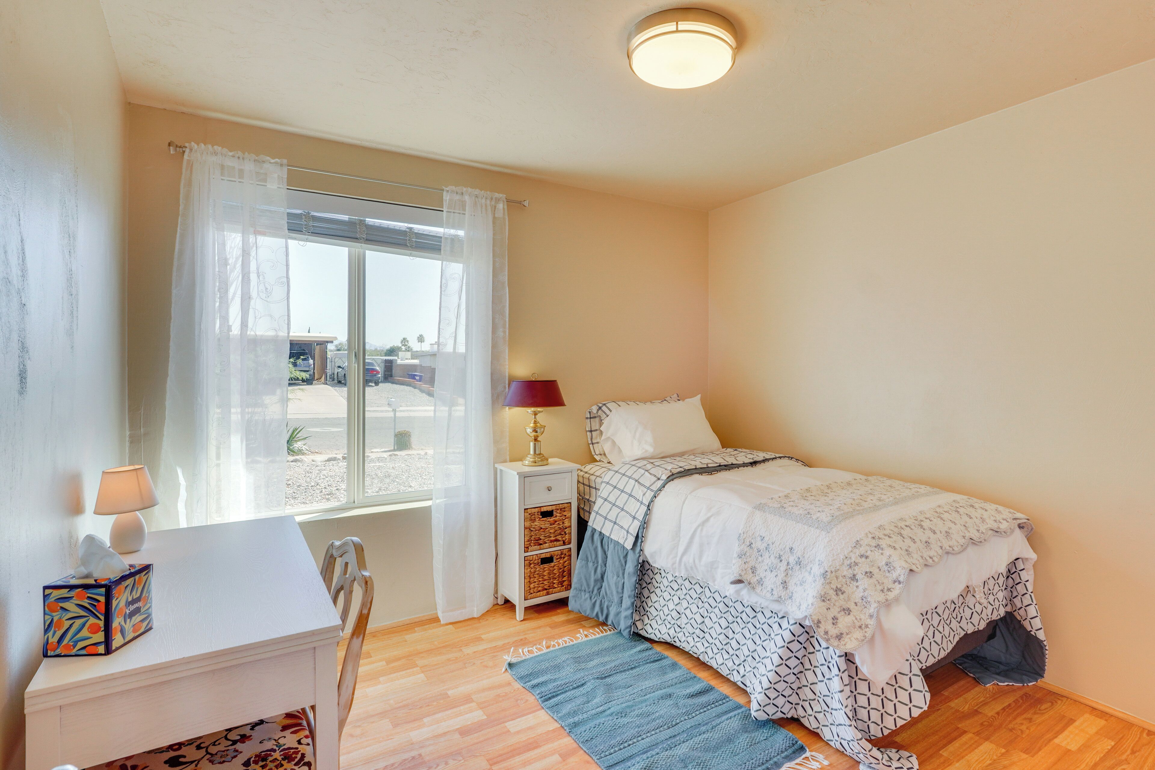 A bedroom with a bed, bedside table, lamp, and window with curtains.
