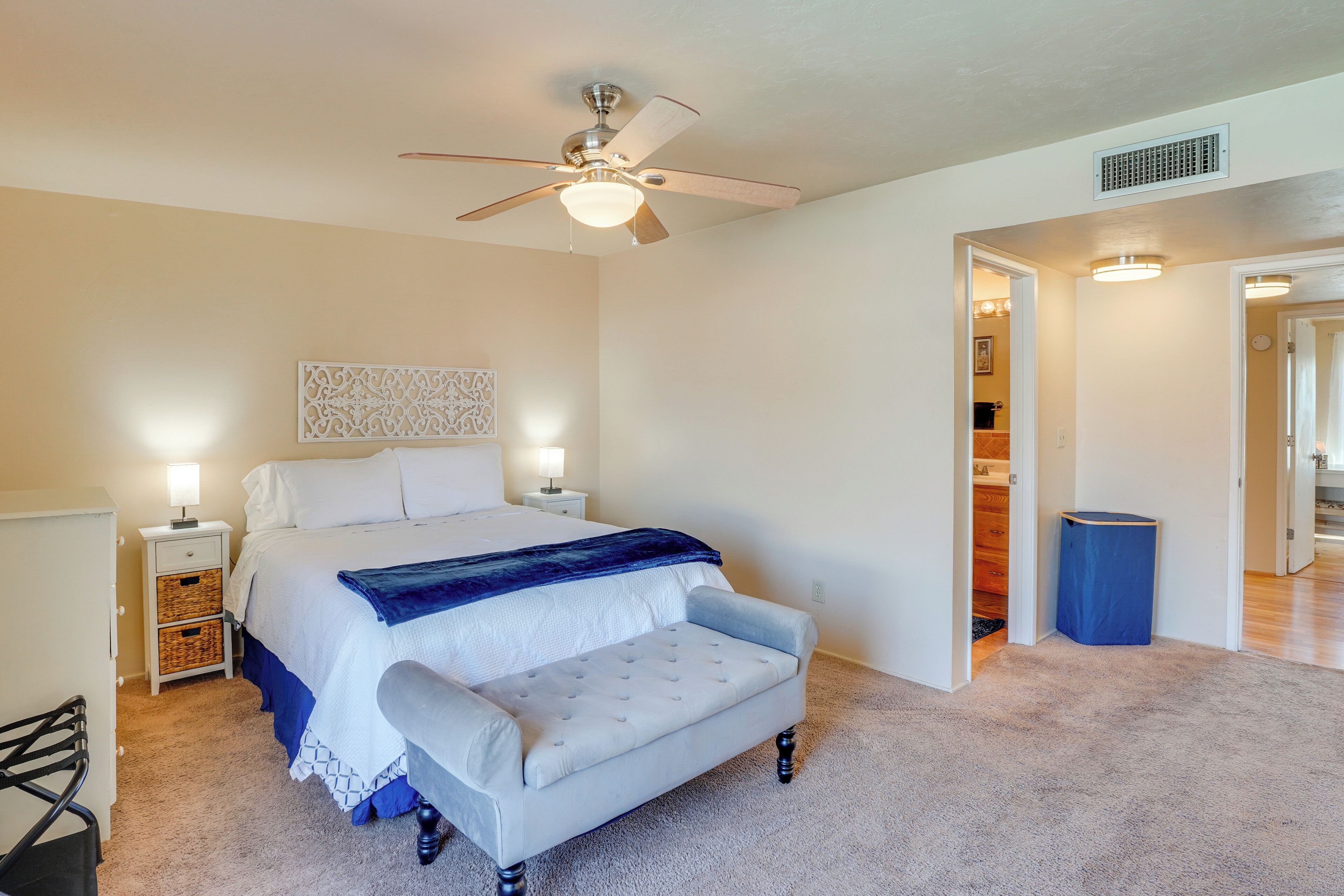 A bedroom with a bed, bedside tables, a ceiling fan, a bench, and a carpeted floor.