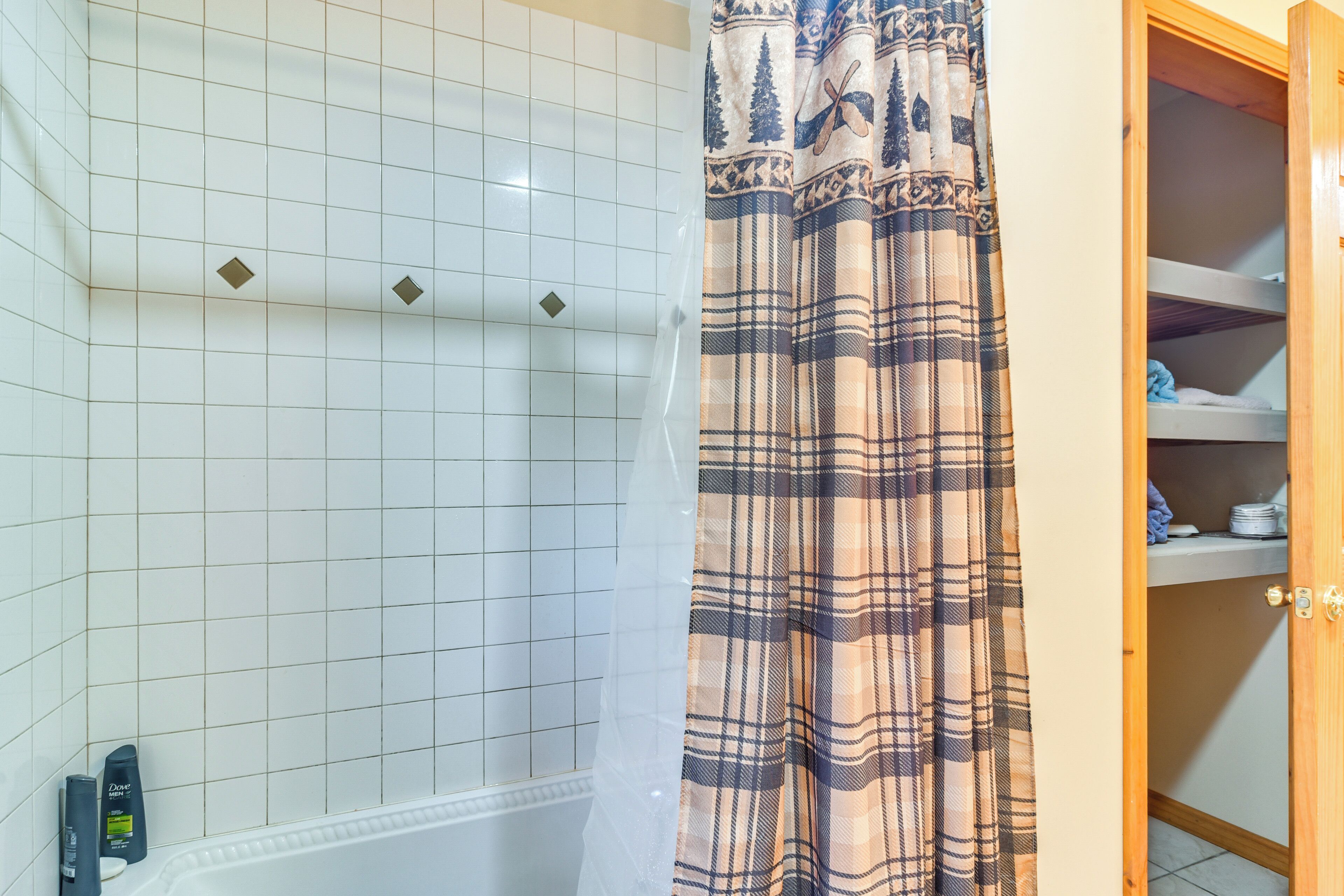 A bathroom with white tiled walls, a shower curtain, and a wooden cabinet with shelves.