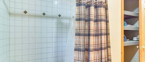 A bathroom with white tiled walls, a shower curtain, and a wooden cabinet with shelves.