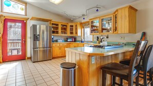A kitchen with wooden cabinets, a stainless steel refrigerator, a tiled floor, and a red door. - Mtn-view Getaway w/ On-site Trails in Fairplay! (Fairplay)