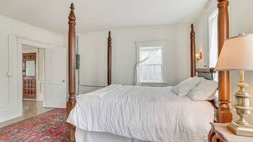 A four-poster bed with white bedding, a red patterned rug, and a wooden nightstand with a lamp.