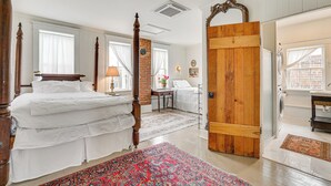 A bedroom with a four-poster bed, a wooden door, a washing machine, and a bathroom with a sink and mirror.