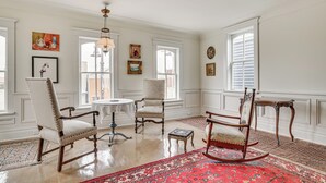 A room with a large window, a chandelier, a round table, and a red patterned rug.