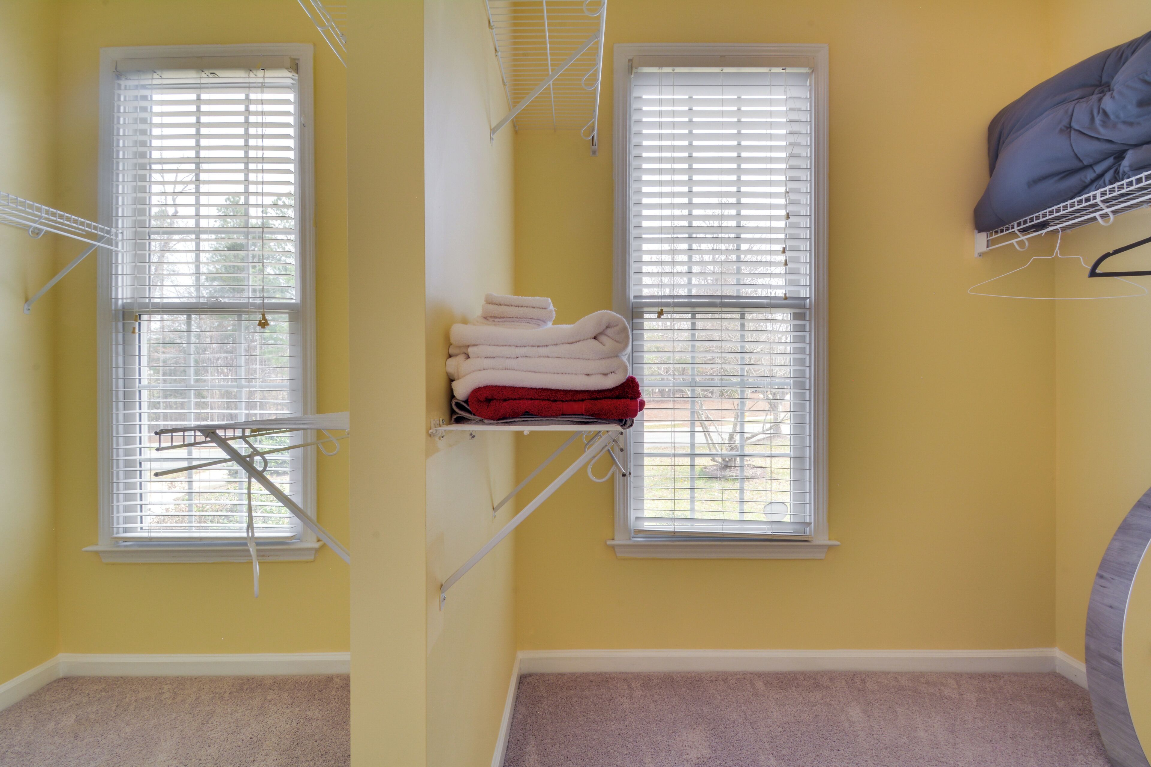 A room with two windows, a towel rack with folded towels, and a hanging coat rack.
