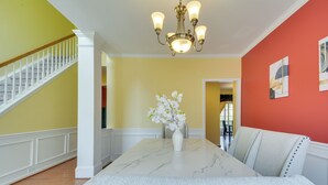 A dining area with a marble table, white upholstered chairs, a vase with white flowers, and a chandelier. - Fire Pit + Pool Access: Quiet Holly Springs Home (Holly Springs)