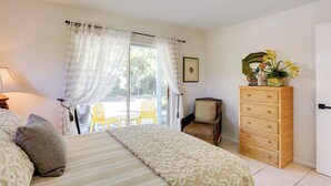 Een slaapkamer met een bed, een rieten dressoir, een stoel en een raam met gordijnen.