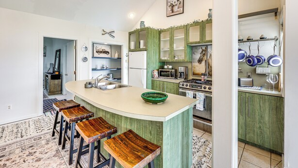 Una cocina con una isla central, taburetes de bar, microondas, estufa y armarios.