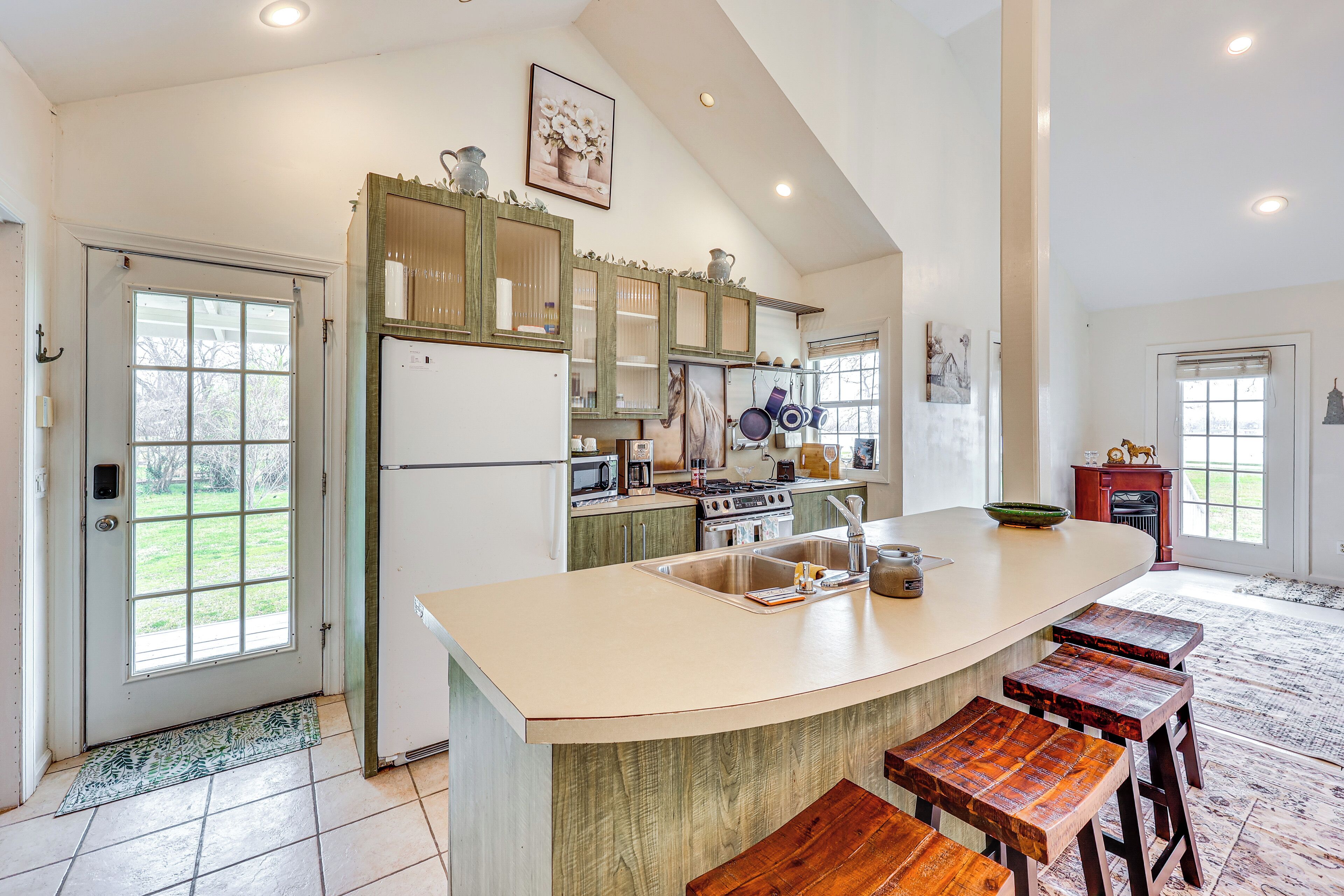 A spacious kitchen with a large island, wooden stools, and a view of the backyard through the door.