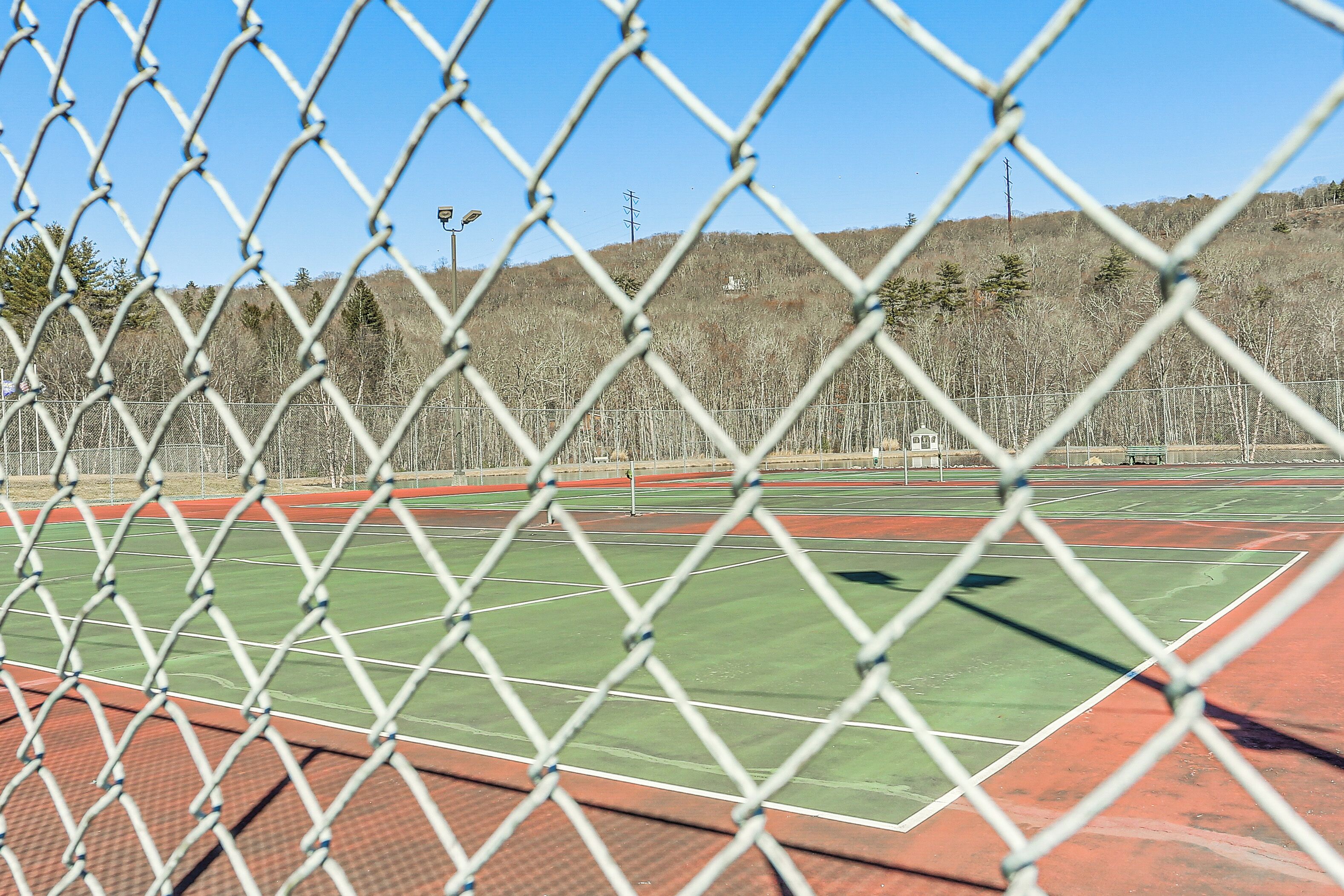 Une clôture en treillis métallique entoure un terrain de tennis dont la surface est rouge et verte.