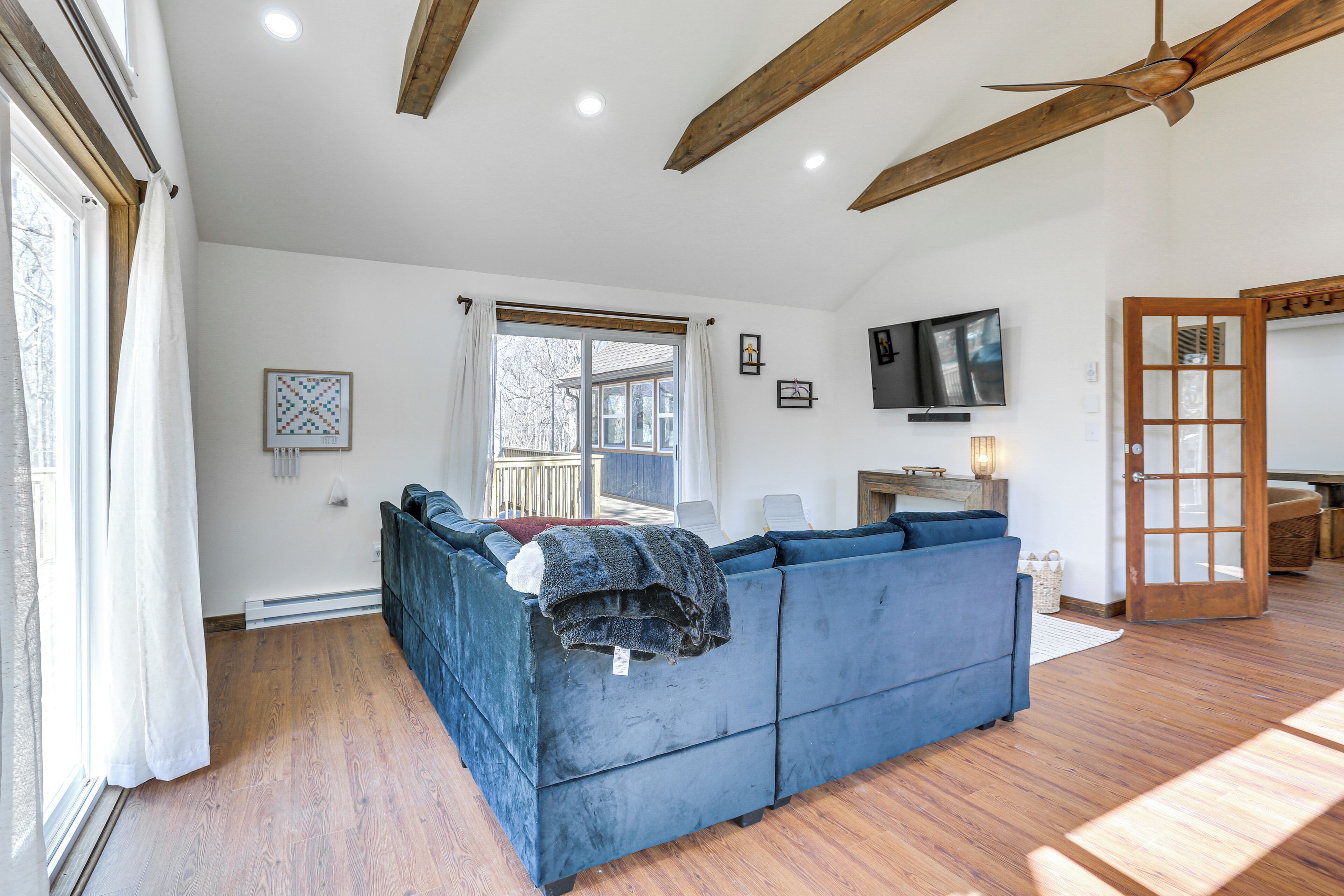 A modern living room with a blue sectional sofa, wooden flooring, a ceiling fan, and a large window.