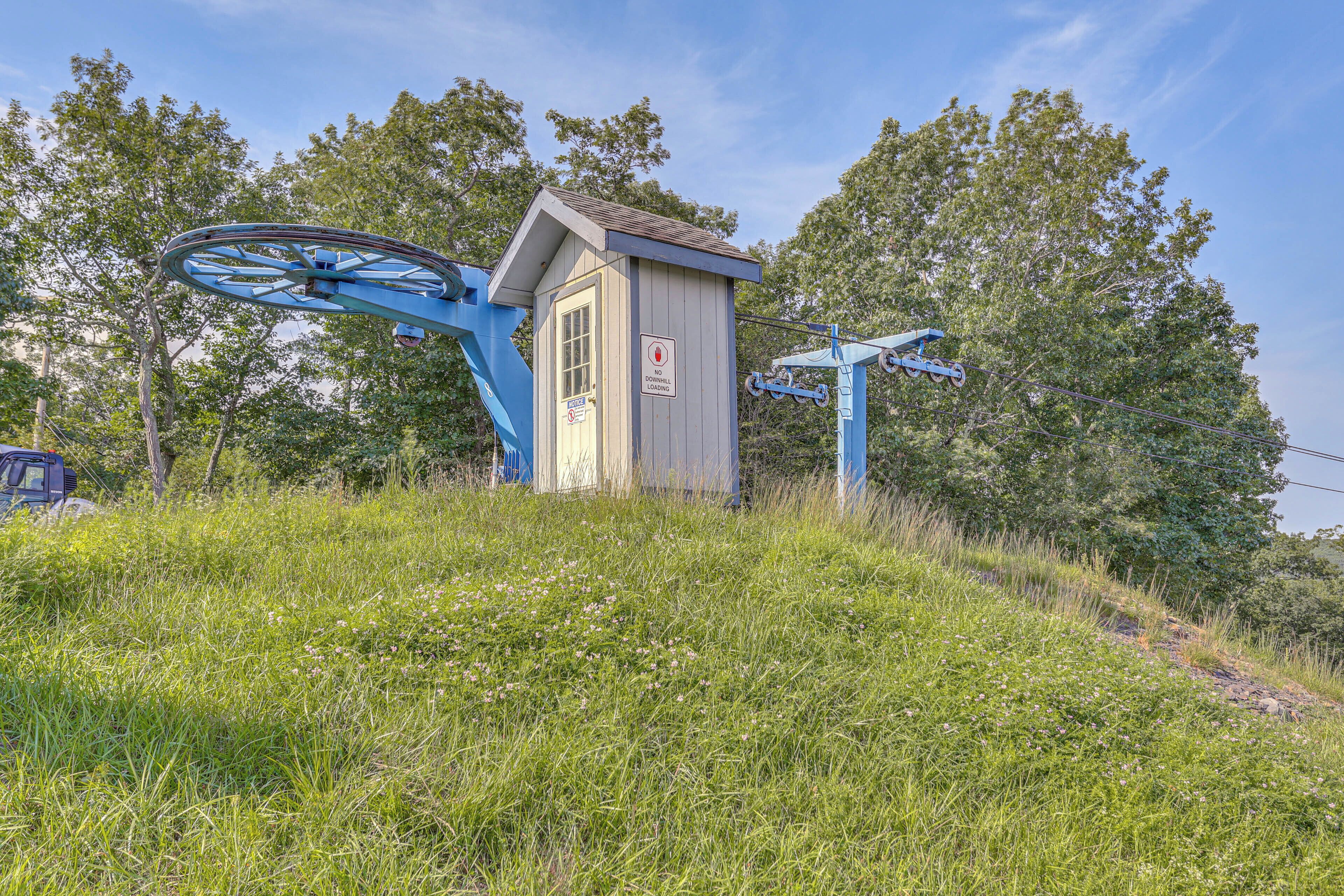 Une petite cabane en bois, dotée d’une structure métallique accolée, entourée d’herbe et d’arbres.