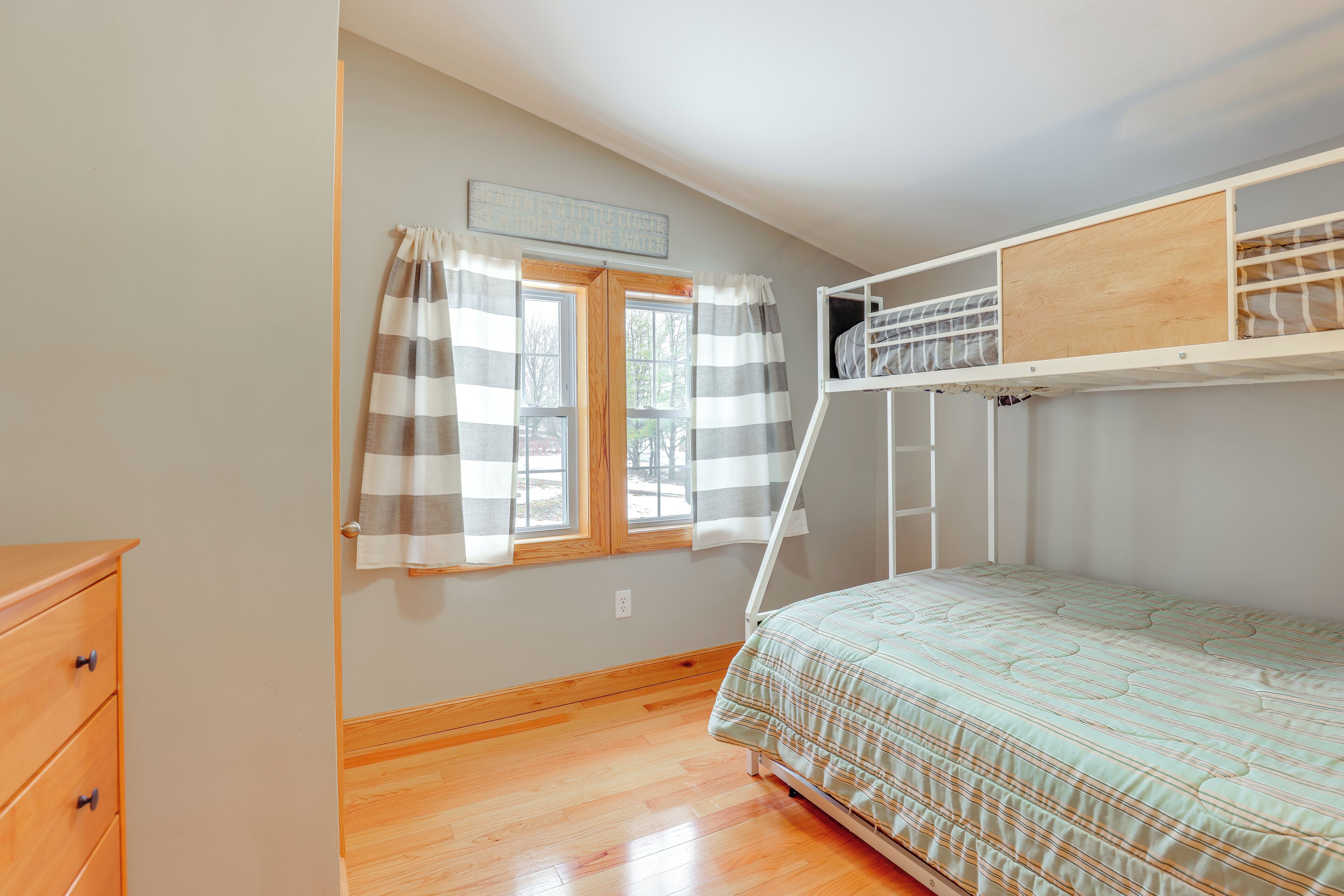 Une chambre avec un lit superposé, une commode en bois, une fenêtre avec des rideaux et un mur de couleur claire.