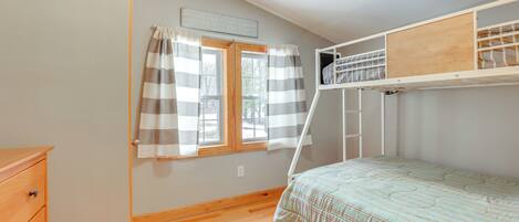 Une chambre avec un lit superposé, une commode en bois, une fenêtre avec des rideaux et un mur de couleur claire.