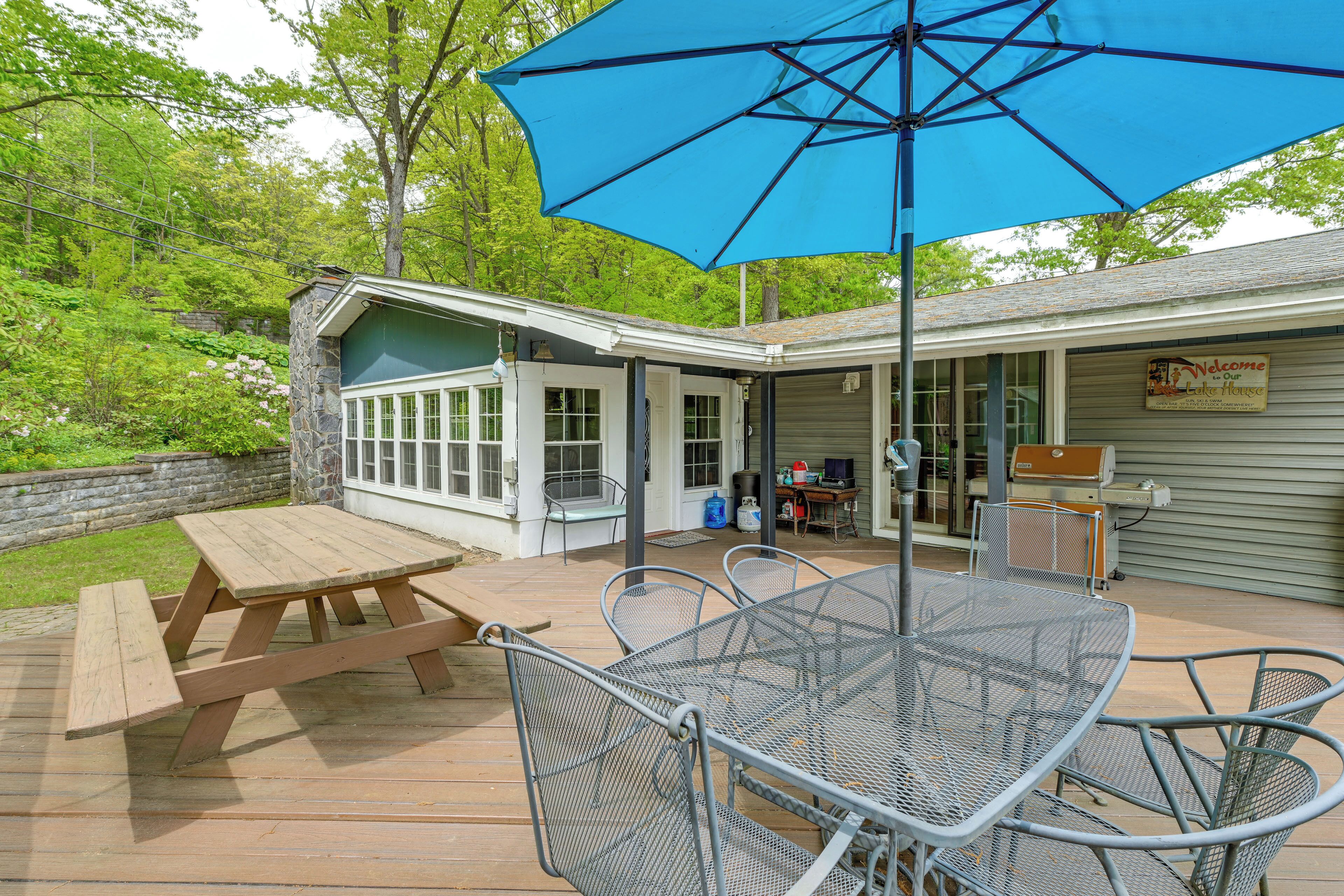 Une terrasse extérieure avec une table et des chaises en bois, un parasol bleu et un barbecue.