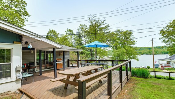 A wooden deck with picnic tables and a blue umbrella, overlooking a lake. - Walk to Lake! Home w/ Private Dock in Alpine (Alpine)