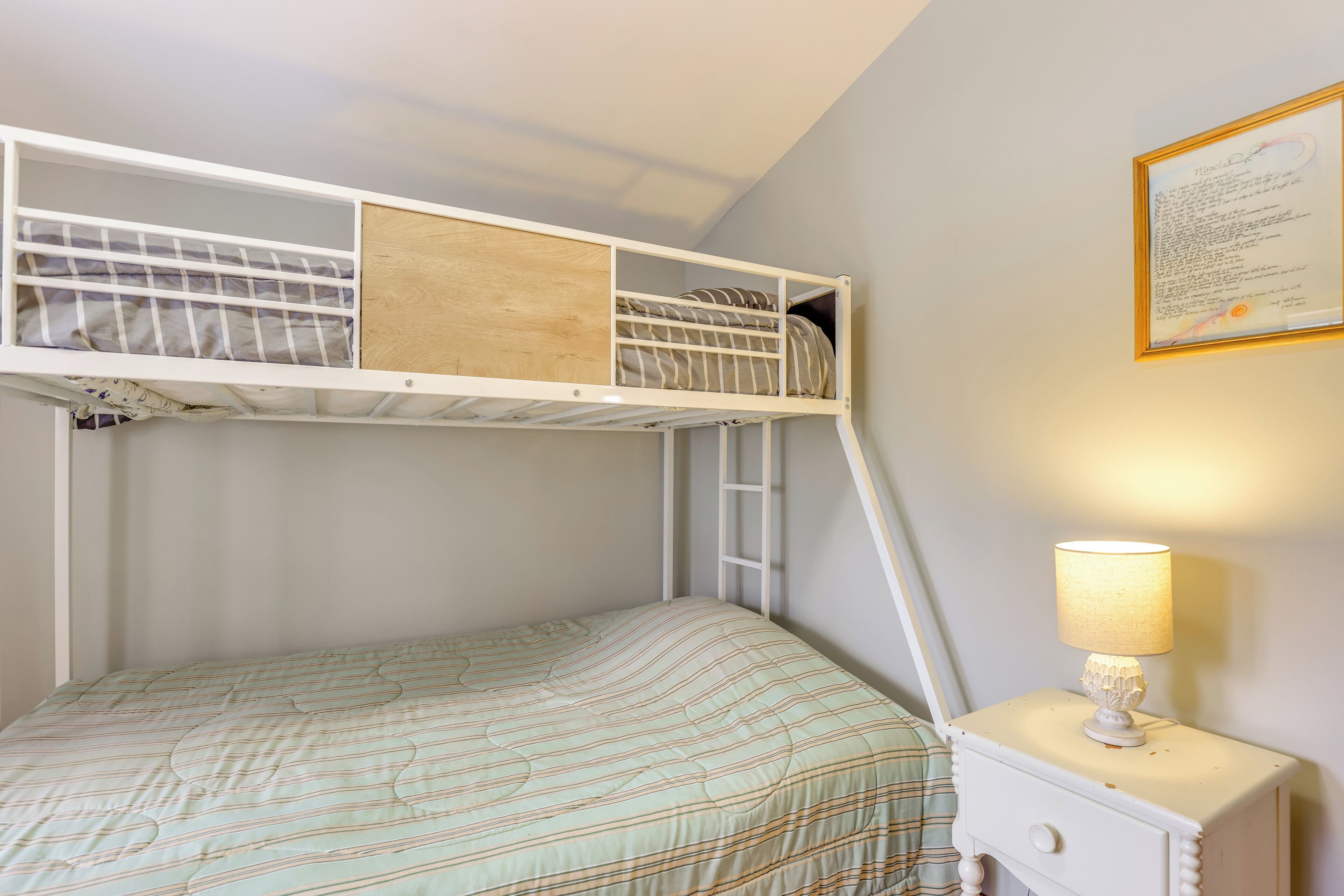 A bunk bed with a ladder, a bedside table with a lamp, and a framed certificate on the wall.