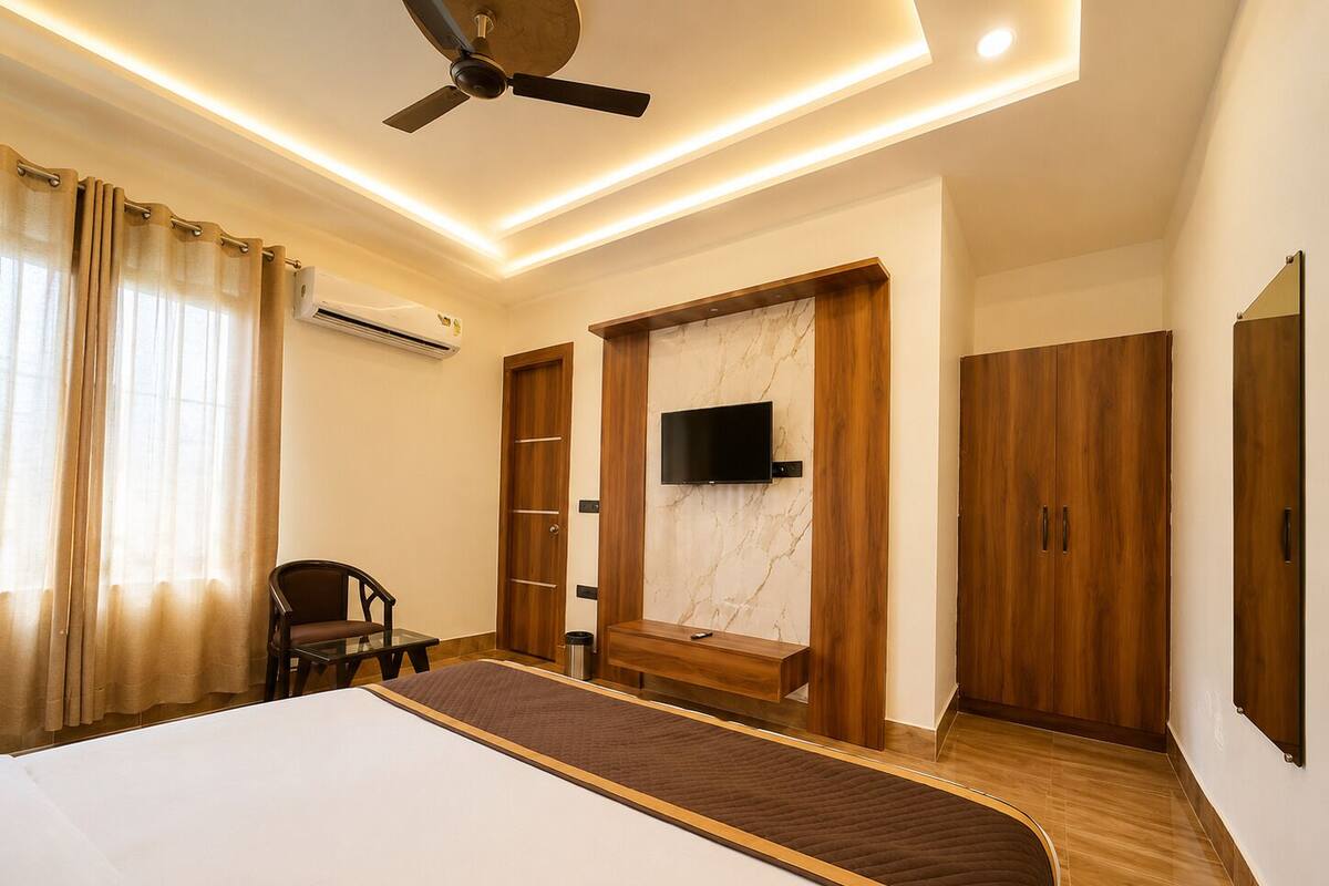 A bedroom with a bed, a ceiling fan, an air conditioning unit, a TV mounted on the wall, wooden wardrobes, and a chair.