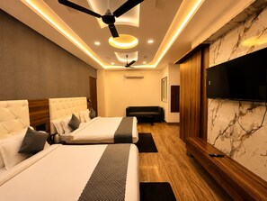 A hotel room with two beds, a ceiling fan, recessed lighting, a flat-screen TV, and a marble-patterned wall.
