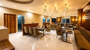 A modern hotel dining area with a long communal table, individual dining tables, and a seating area with sofas. - The Vrindavan Inn (Vrindavan)