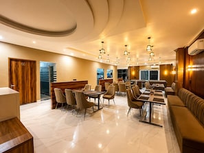 A modern hotel dining area with a long communal table, individual dining tables, and a seating area with sofas. - The Vrindavan Inn (Vrindavan)