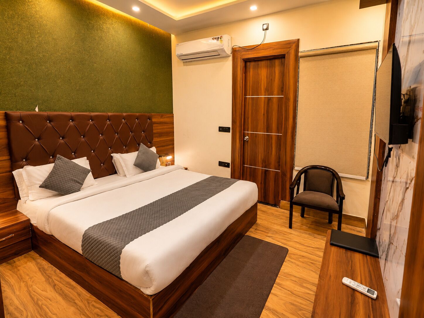 A neatly arranged hotel room with a large bed, a wooden wardrobe, a chair, and a wall-mounted TV.