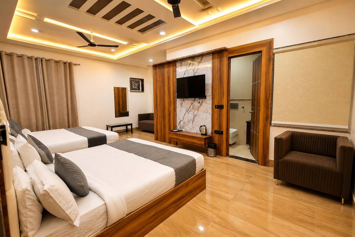 A hotel room with two beds, a TV, a wooden desk, a chair, and a bathroom visible through an open door.