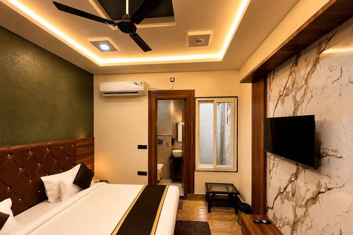 A hotel room with a bed, ceiling fan, air conditioning unit, TV, and a view of the outside through a window.