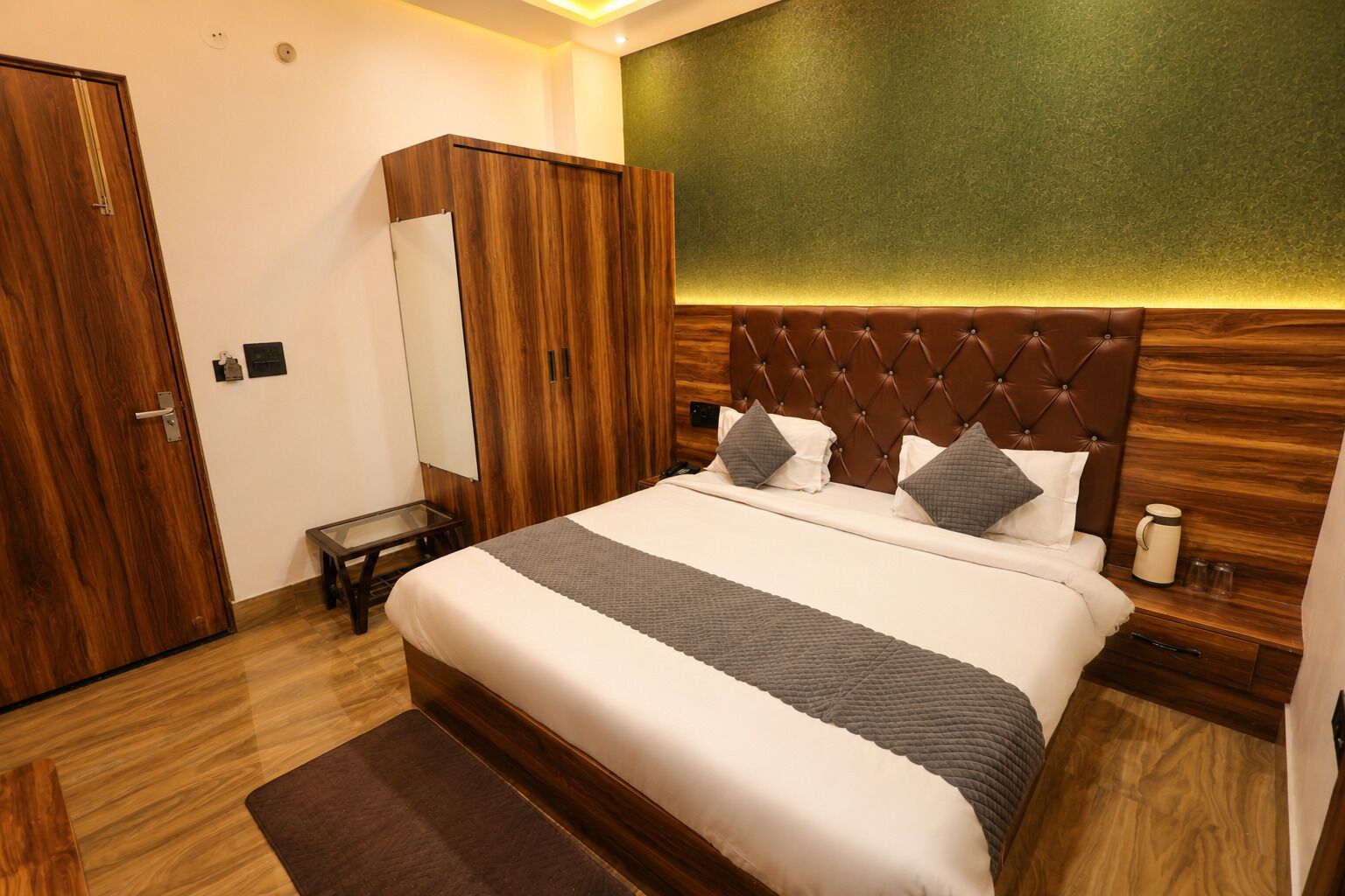 Una camera d'albergo con un letto, un armadio in legno, un comodino e una parete verde decorativa.