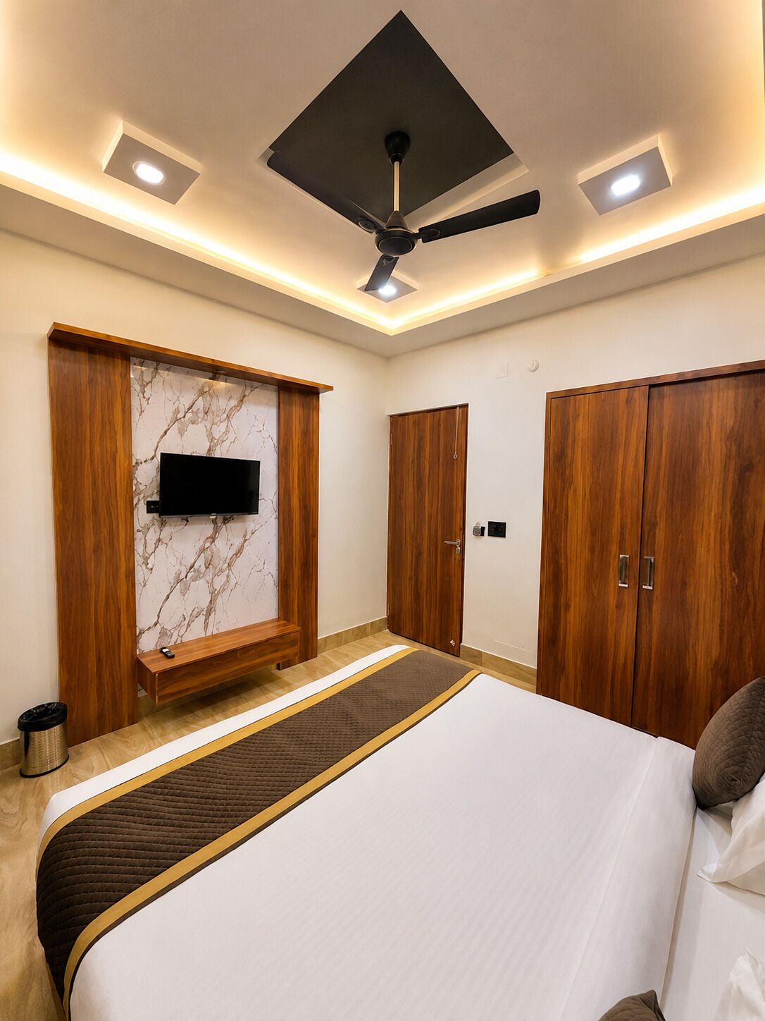Un dormitorio con una cama, ventilador de techo, televisor montado en la pared y armarios de madera.